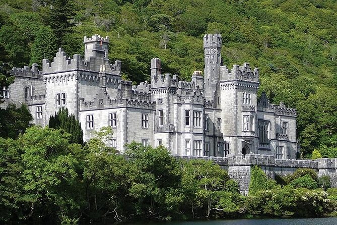 The granite battlements and tall corner tower of Kylemore Abbey against the woods