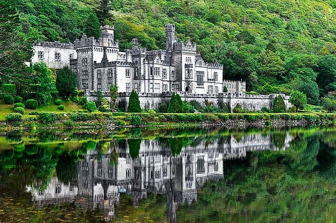 Kylemore Abbey and its reflection in the lough, below a wooded mountainside