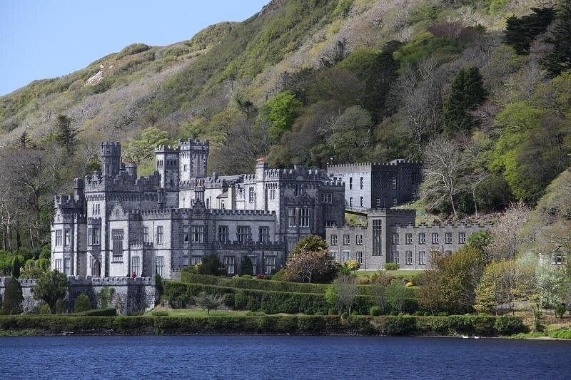 The long front of Kylemore Abbey on the lakeshore, under a bare spring mountainside