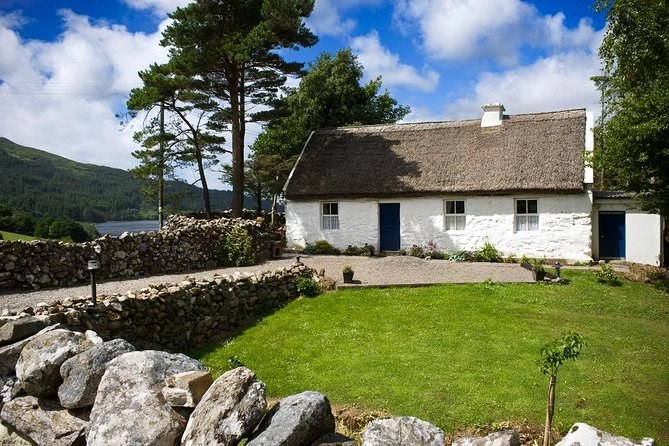 A whitewashed thatched cottage behind dry stone walls and a lawn