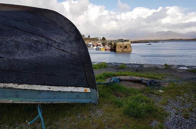 An upturned black currach on the shore, with a small harbour behind
